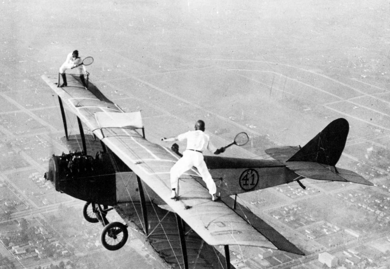 detajl z naslovnice Ekran x Maska: dva pilota igrata tenis na krilih starinskega letala