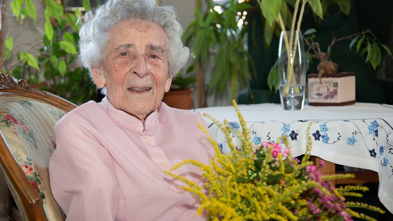 Emilija s sivimi lasmi in roza bluzo, obkrožena s šopki rož