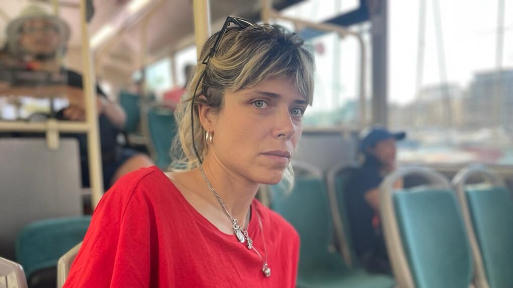 Hana Jušič v rdeči majici s kratkimi rokavi, slikana na mestnem avtobusu